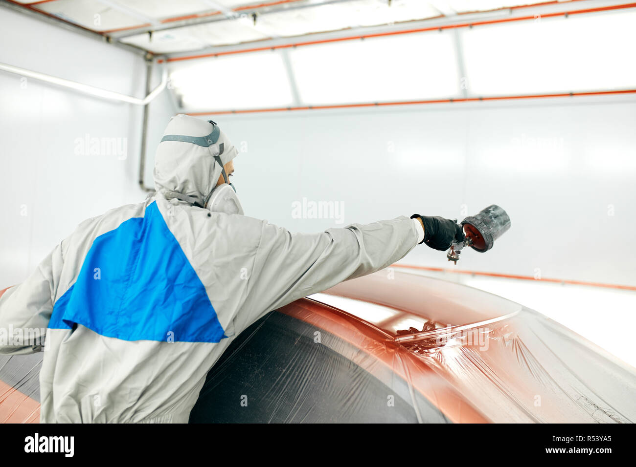 auto painter in protective workwear and respirator painting car body in paint chamber Stock