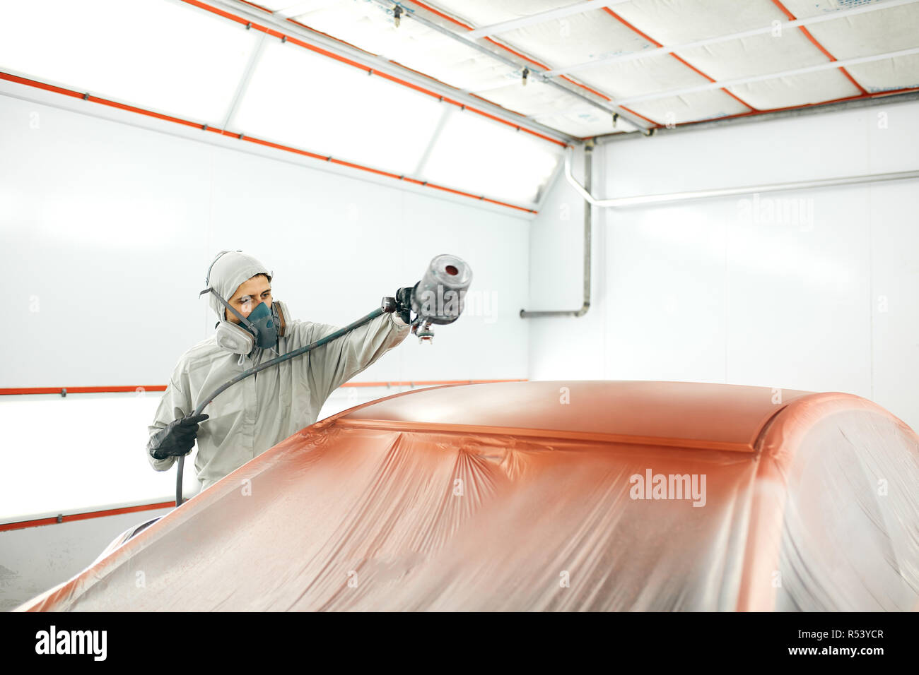 auto painter in protective workwear and respirator painting car body in