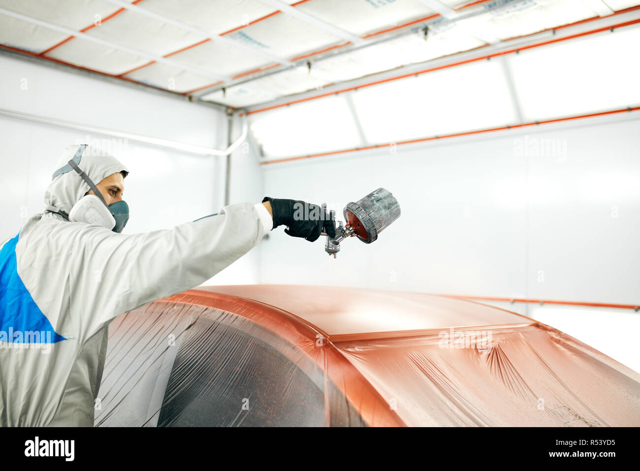 auto painter in protective workwear and respirator painting car body in
