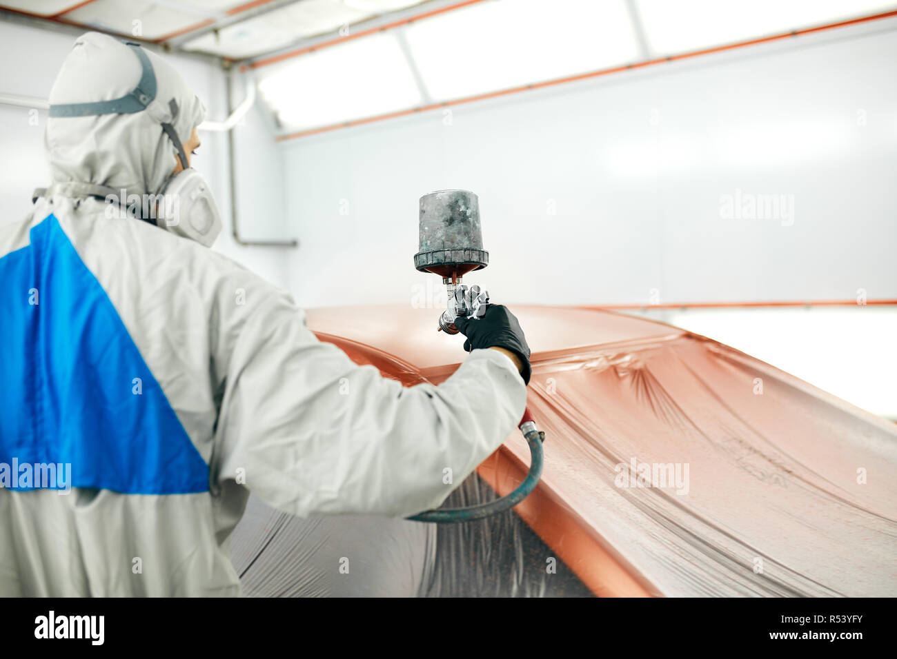 auto painter in protective workwear and respirator painting car body in
