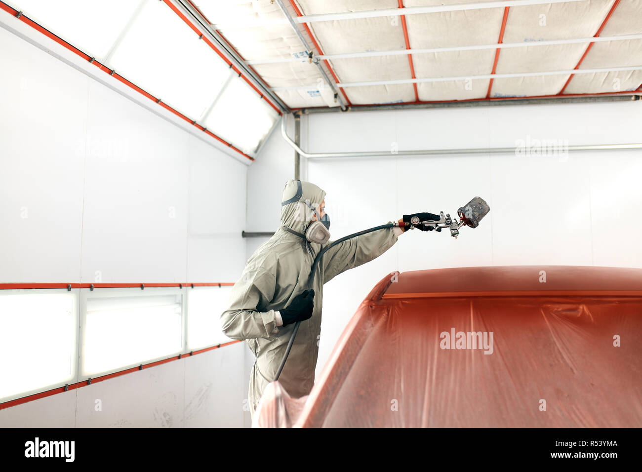auto painter in protective workwear and respirator painting car body in