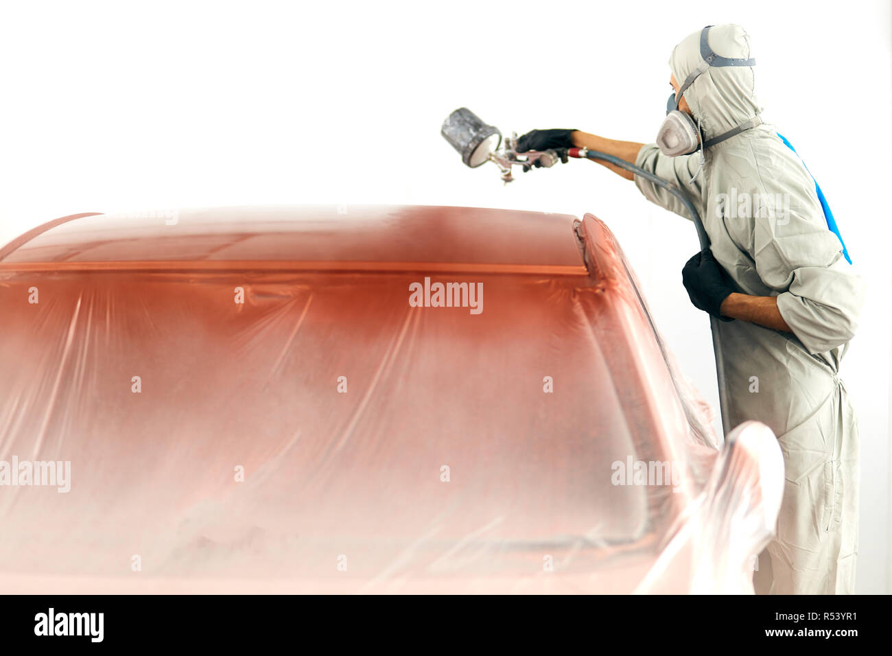 auto painter in protective workwear and respirator painting car body in