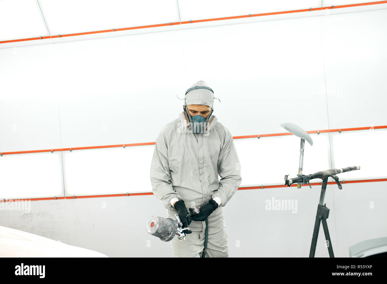 auto painter in protective workwear and respirator painting car body in paint chamber Stock