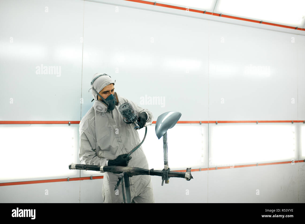 auto painter in protective workwear and respirator painting car body in paint chamber Stock