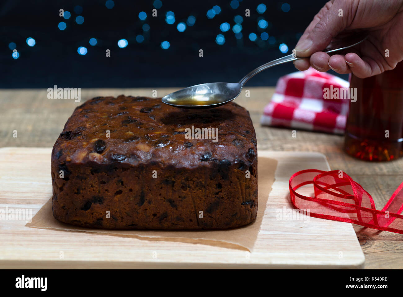 'Feeding' a traditional rich fruit Christmas cake by pouring a spoonful of brandy over it Stock