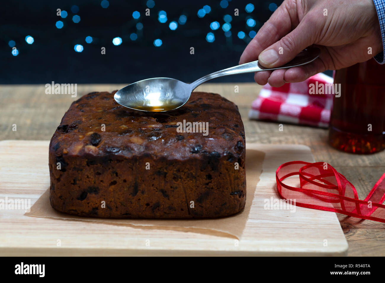 'Feeding' a traditional rich fruit Christmas cake by pouring a spoonful of brandy over it. Stock Photo