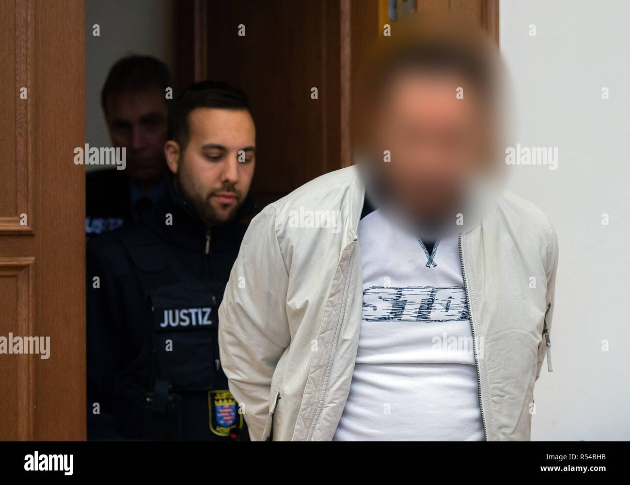 27 November 2018, Hessen, Gießen: The 48-year-old defendant (r) is taken to the courtroom of the Regional Court by judicial officers before the trial begins. About three years ago, the son of the billionaire Würth was kidnapped. Together with accomplices, the accused is said to have kidnapped the handicapped son of the Baden-Württemberg entrepreneur Reinhold Würth in June 2015 in Schlitz, East Hesse, and demanded a ransom of three million euros. After a failed handover the victim was found one day later in a forest near Würzburg, unharmed and chained to a tree. Photo: Silas Stein/dpa - ATTENT Stock Photo