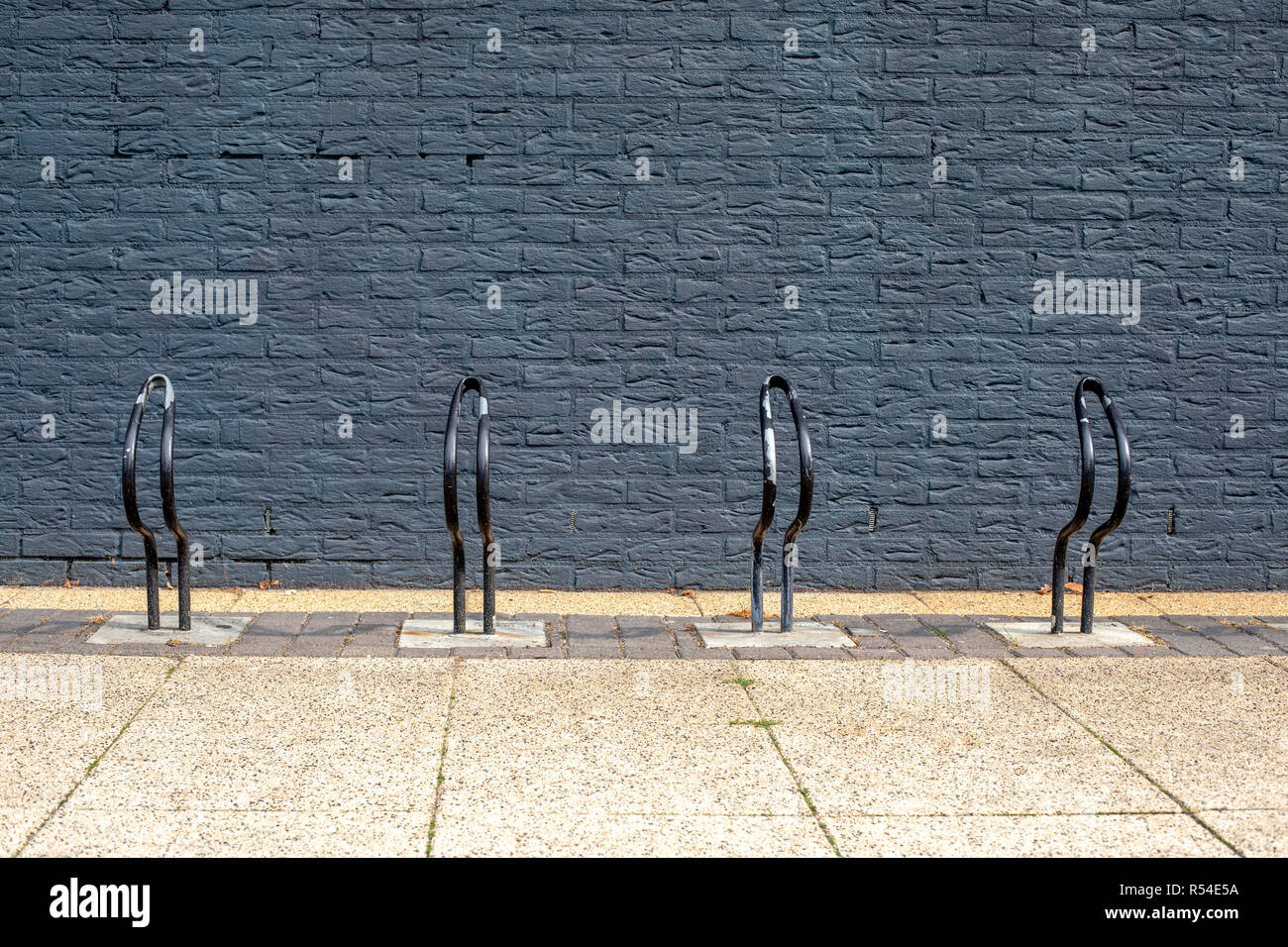 Very simple bike, bicycle racks, painted black in front of a black brick wall. Stock Photo