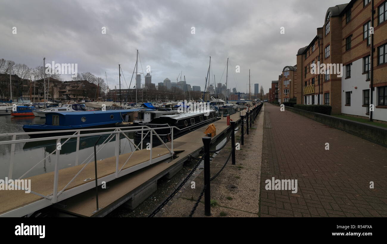 Cloudy Sunday Morning in London South Dock area with lots of parked boats. Walking path on the side with leaving buildings.Grey sky, End of the Autumn Stock Photo