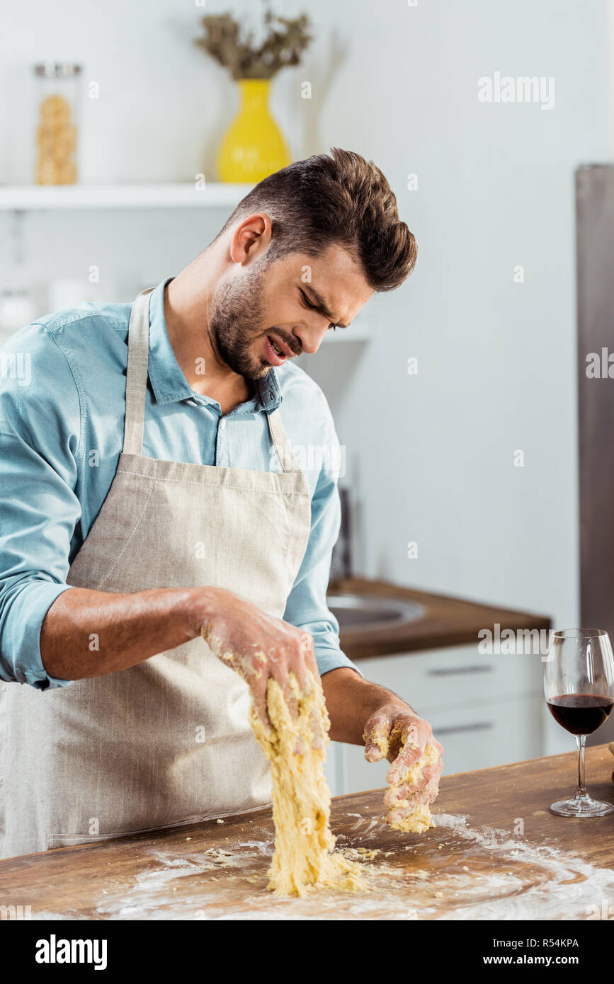 frustrated young man in apron looking at spoiled dough on hands in kitchen  Stock Photo - Alamy