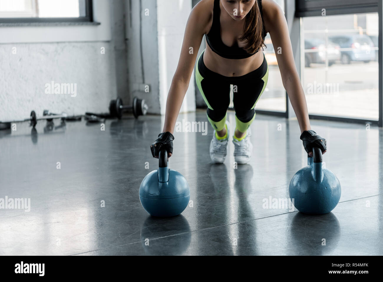 determined sportswoman in weightlifting gloves doing plank exercise on kettlebells at sports center Stock Photo