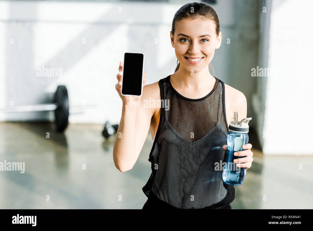 beautiful smiling sportswoman holding sport bottle and smartphone with ...