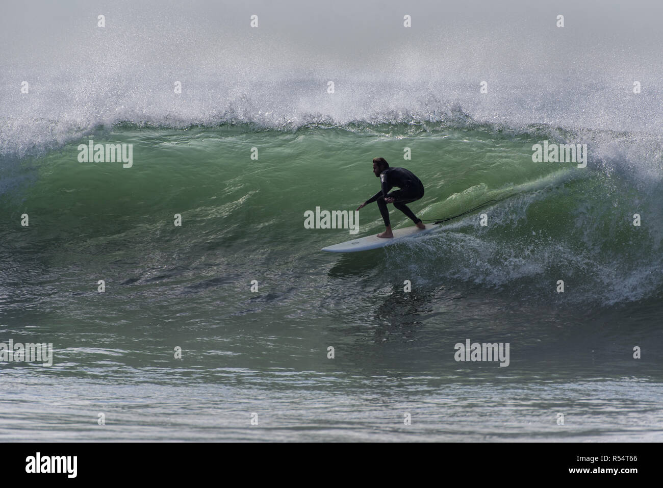 Surfer in low crouch as he ducks under the backlit wave lip in Ventura, California, USA during a late Autumn swell on November 28, 2018. Stock Photo