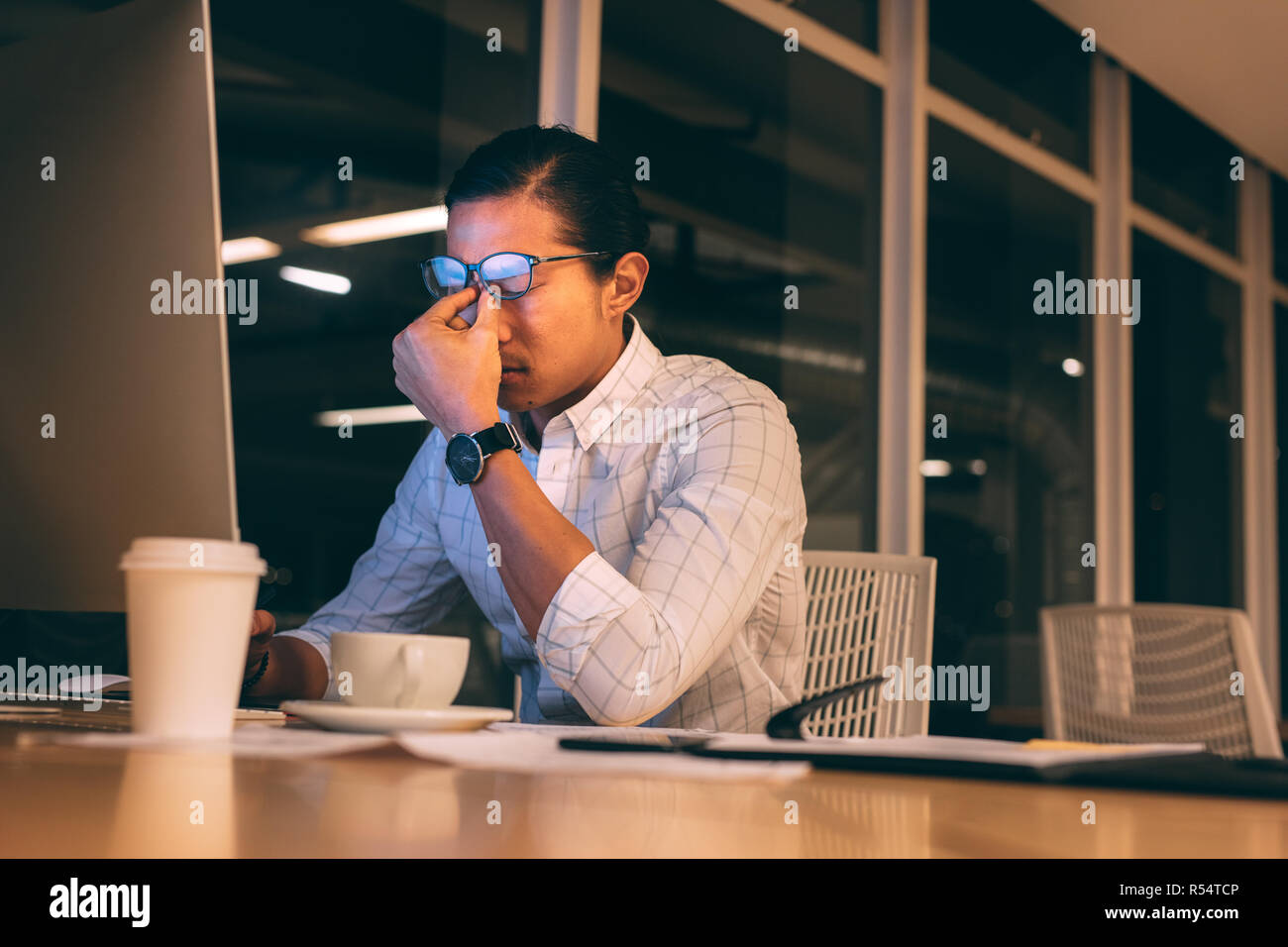 businessman looking tired working late night in office. Man sitting in front of computer working late looking stressed out. Stock Photo