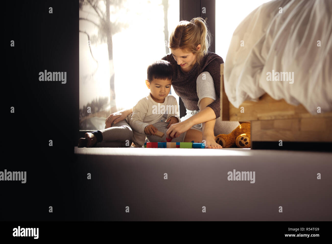 Mother and son playing with toys in bedroom. Young woman with her son playing block games. Stock Photo