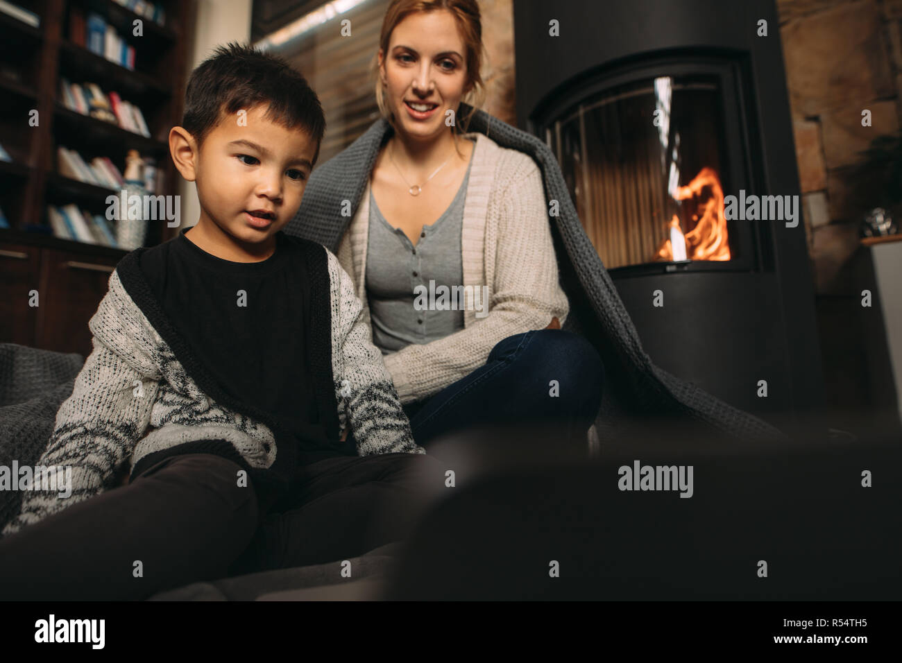 Little boy sitting on floor with his mother and looking at laptop. Son with his mother watching cartoon movie on laptop while sitting near fireplace i Stock Photo