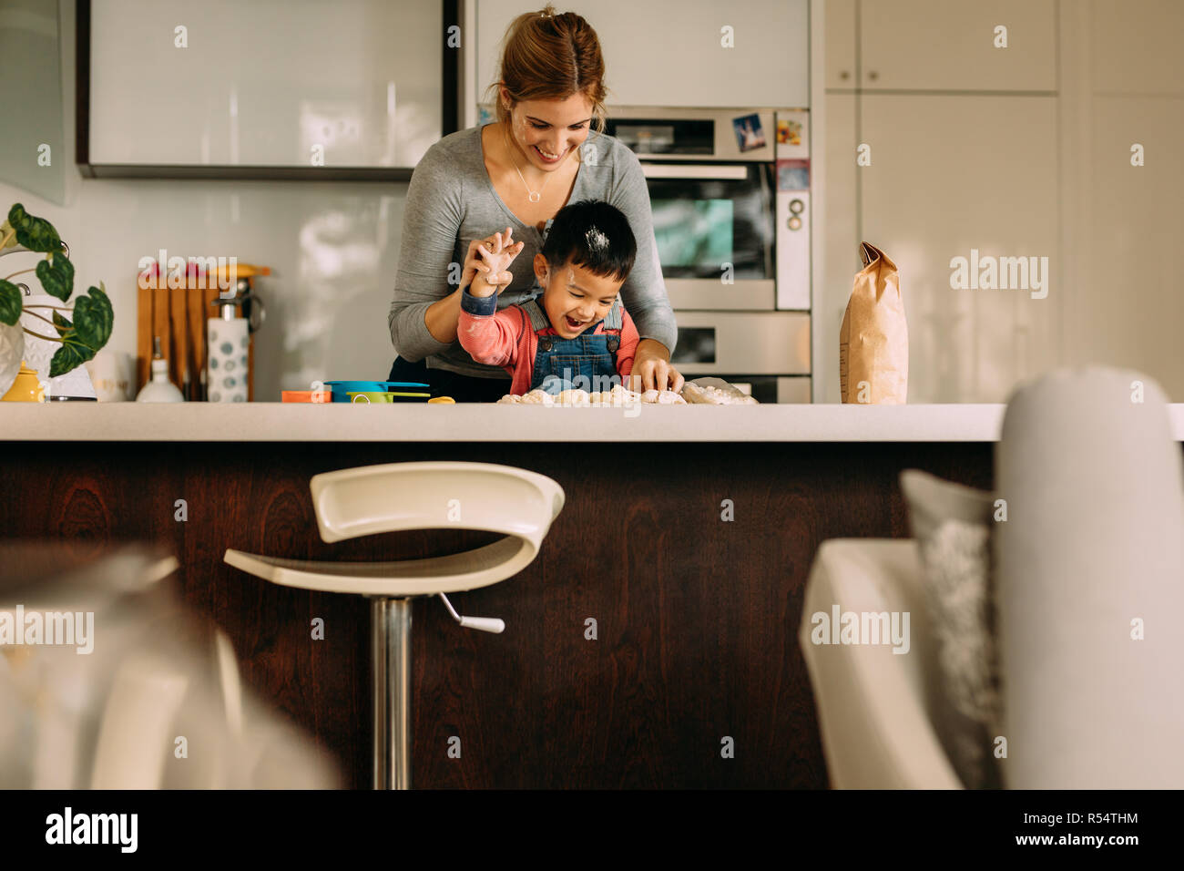 Cheerful little boy enjoying with mother making cookie in kitchen. Mother and son having fun while making cookies at home. Stock Photo