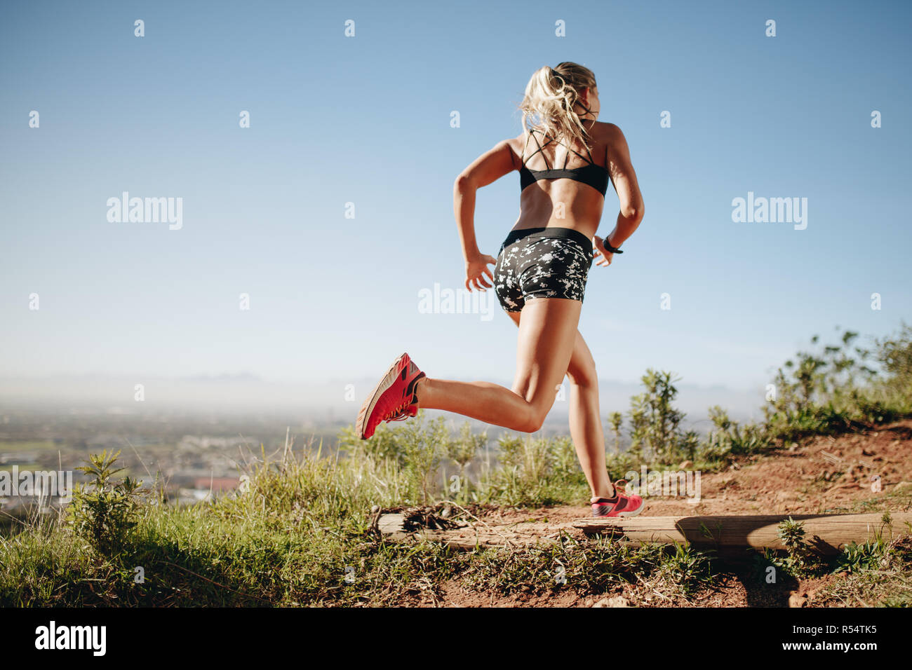 Rear view of a woman in fitness wear sprinting. Female athlete training outdoors running on a sunny day. Stock Photo