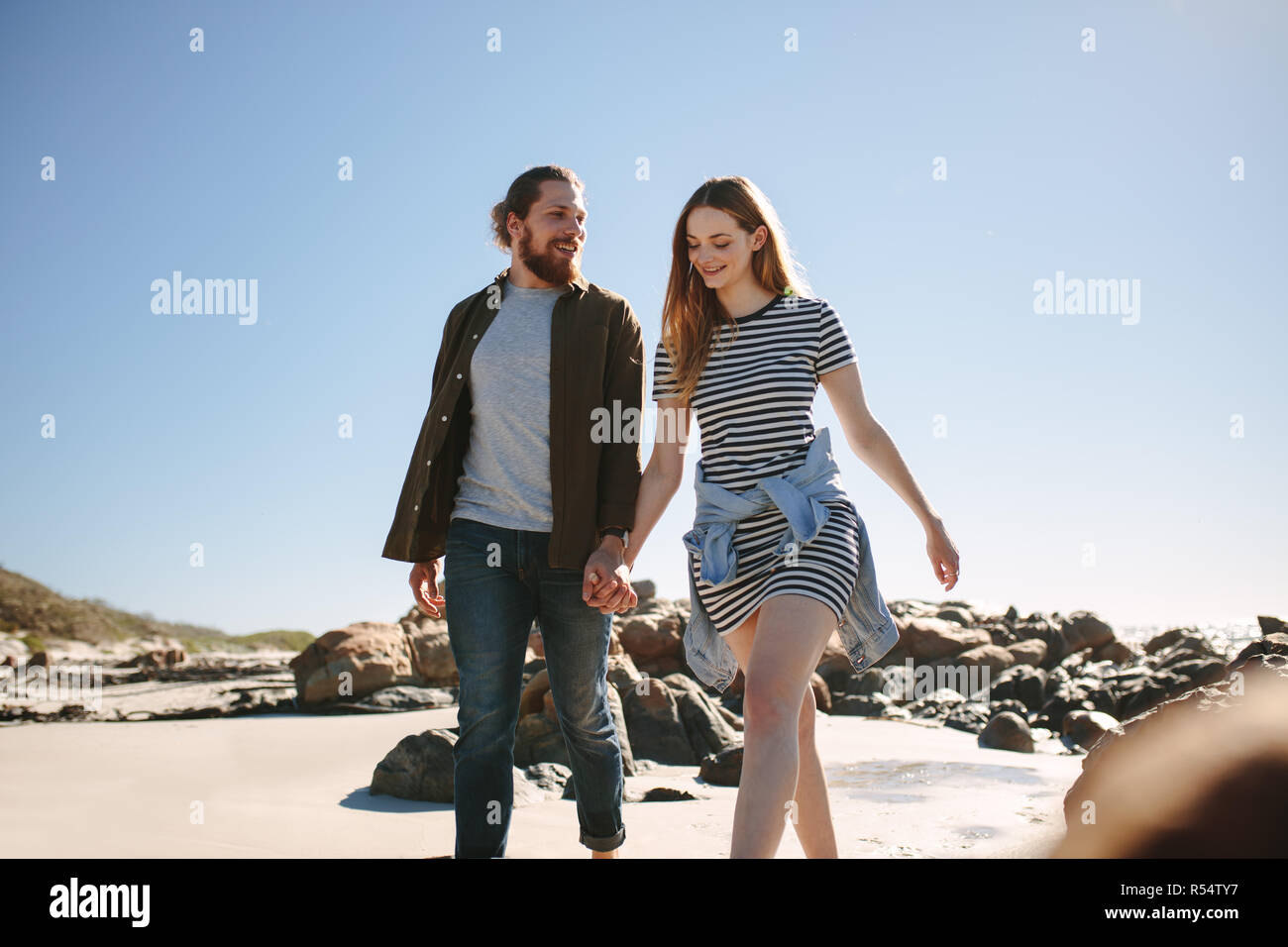 Beautiful couple strolling along a rocky beach. Man and woman walking with hand in hand on the shore. Stock Photo