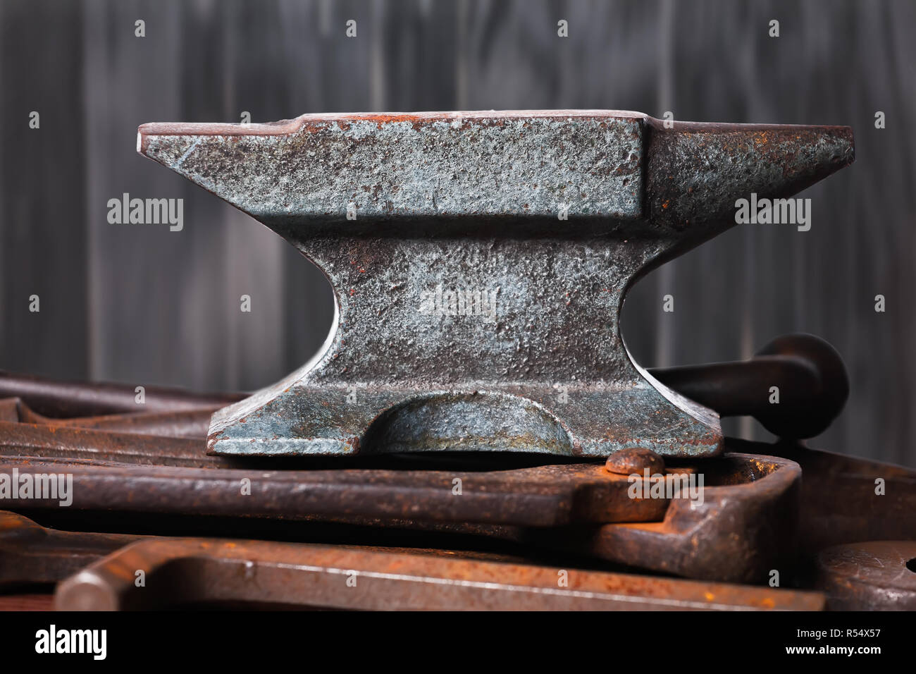 Old rusty rugged anvil on top of other blacksmith tools on black wooden