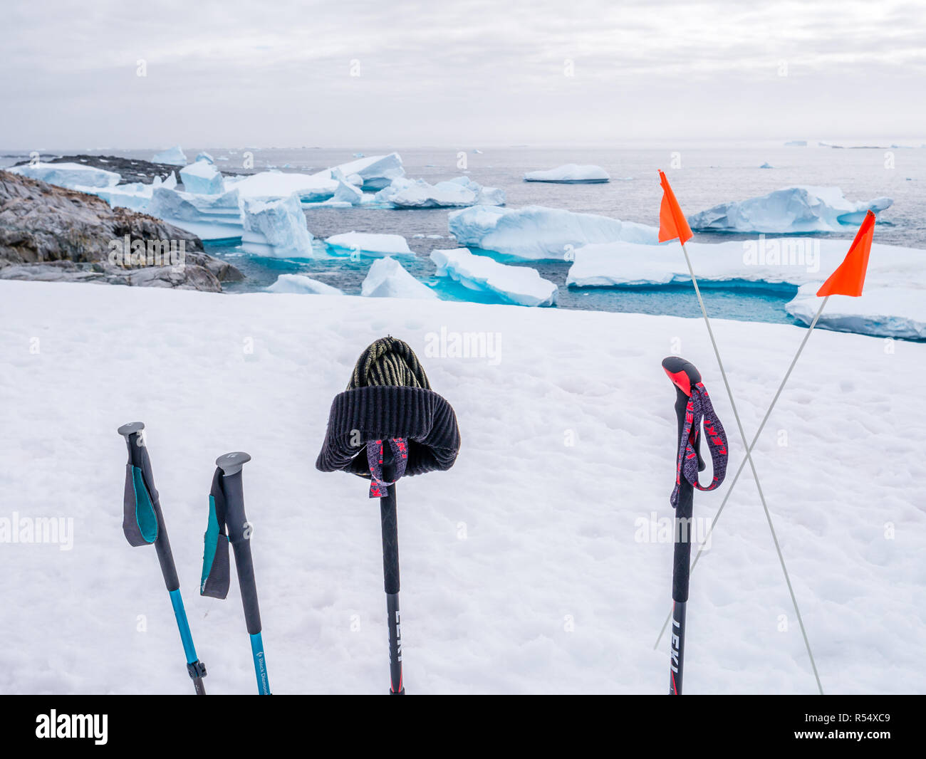 Walking sticks and flags in snow on top of hill on Petermann Island and icebergs in background, Antarctic Peninsula, Antarctica Stock Photo