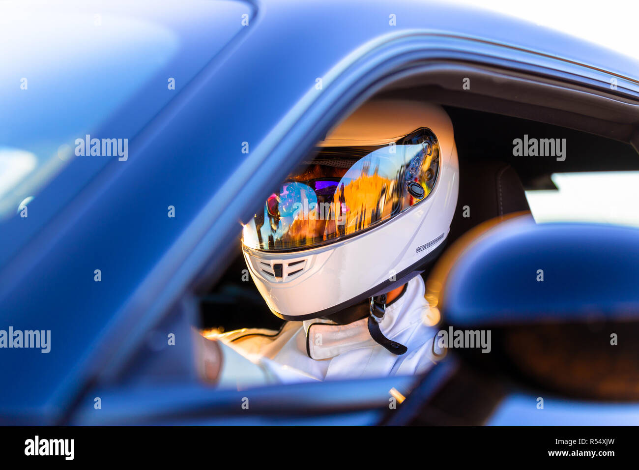 A race car driver wearing a helmet at the wheel of his vehicle on a sunny morning at the track Stock Photo