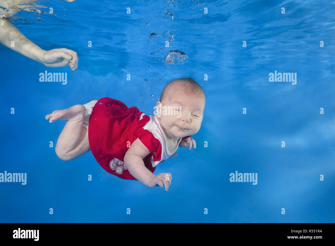 1.5 months girl in a red dress swims underwater in the pool, mother holding the child. Healthy family lifestyle and children water sports activity. Ch Stock Photo