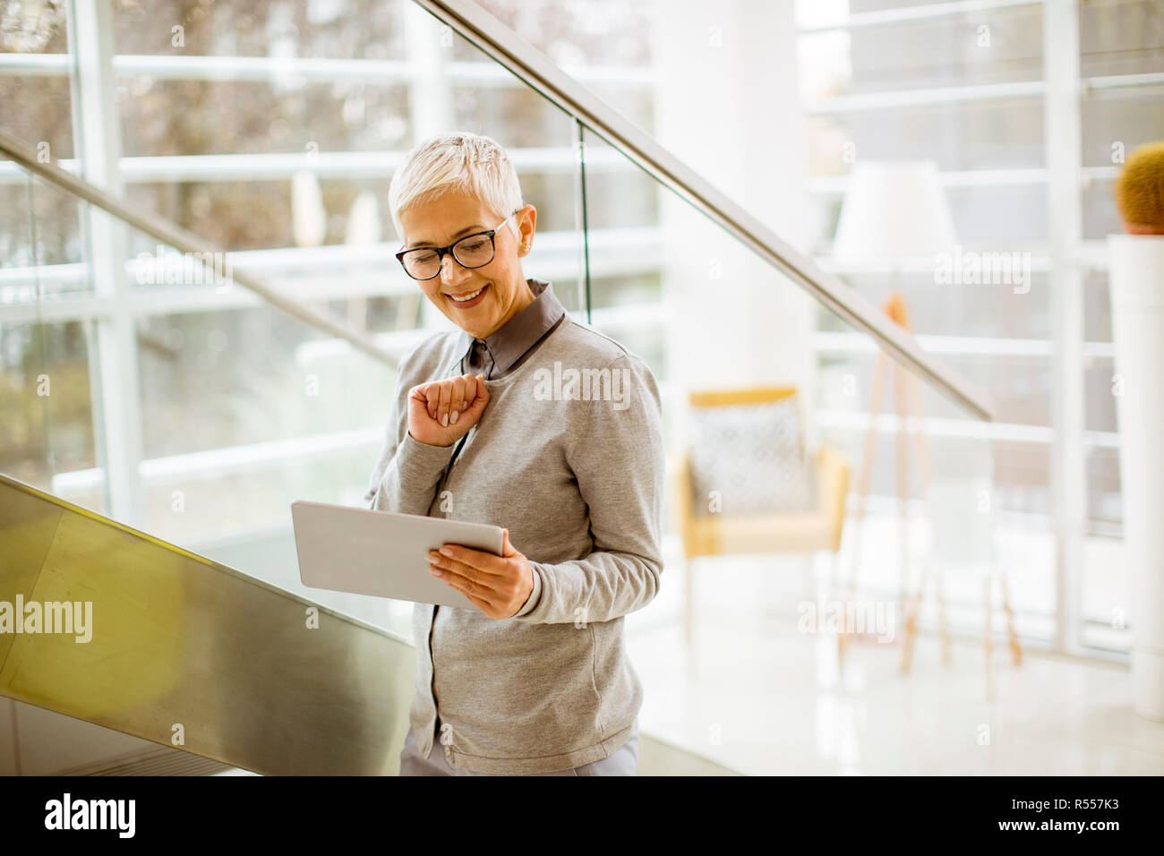 Pretty, positive, aged woman with beaming smile holding tablet in modern office Stock Photo