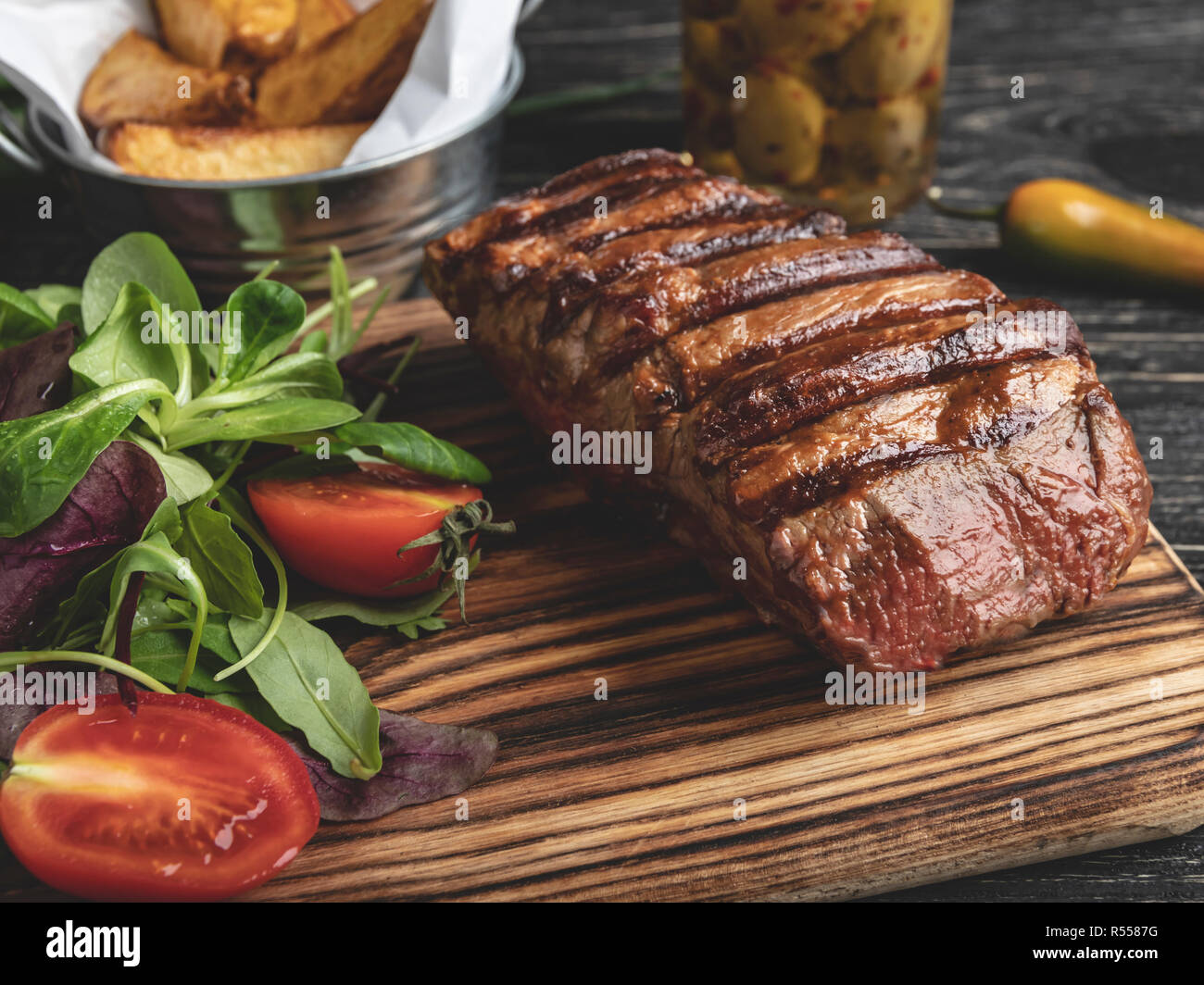 steak on the board with herbs, fried potatoes, spices on a black surface Stock Photo