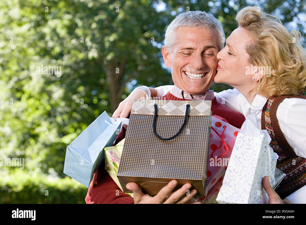 Wife kissing husband with bags of gifts Stock Photo