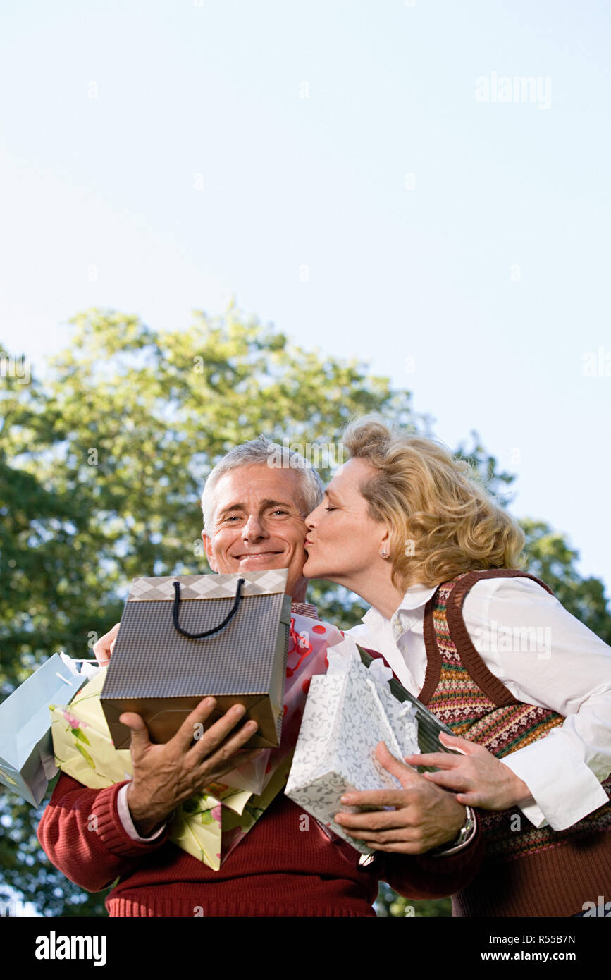 Wife kissing husband with bags of gifts Stock Photo