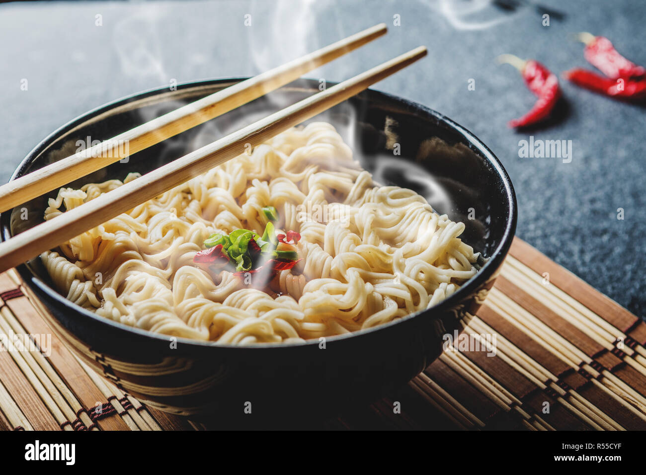 Black bowl of asian instant noodles with hot water and red chili peppers and green onion Stock Photo
