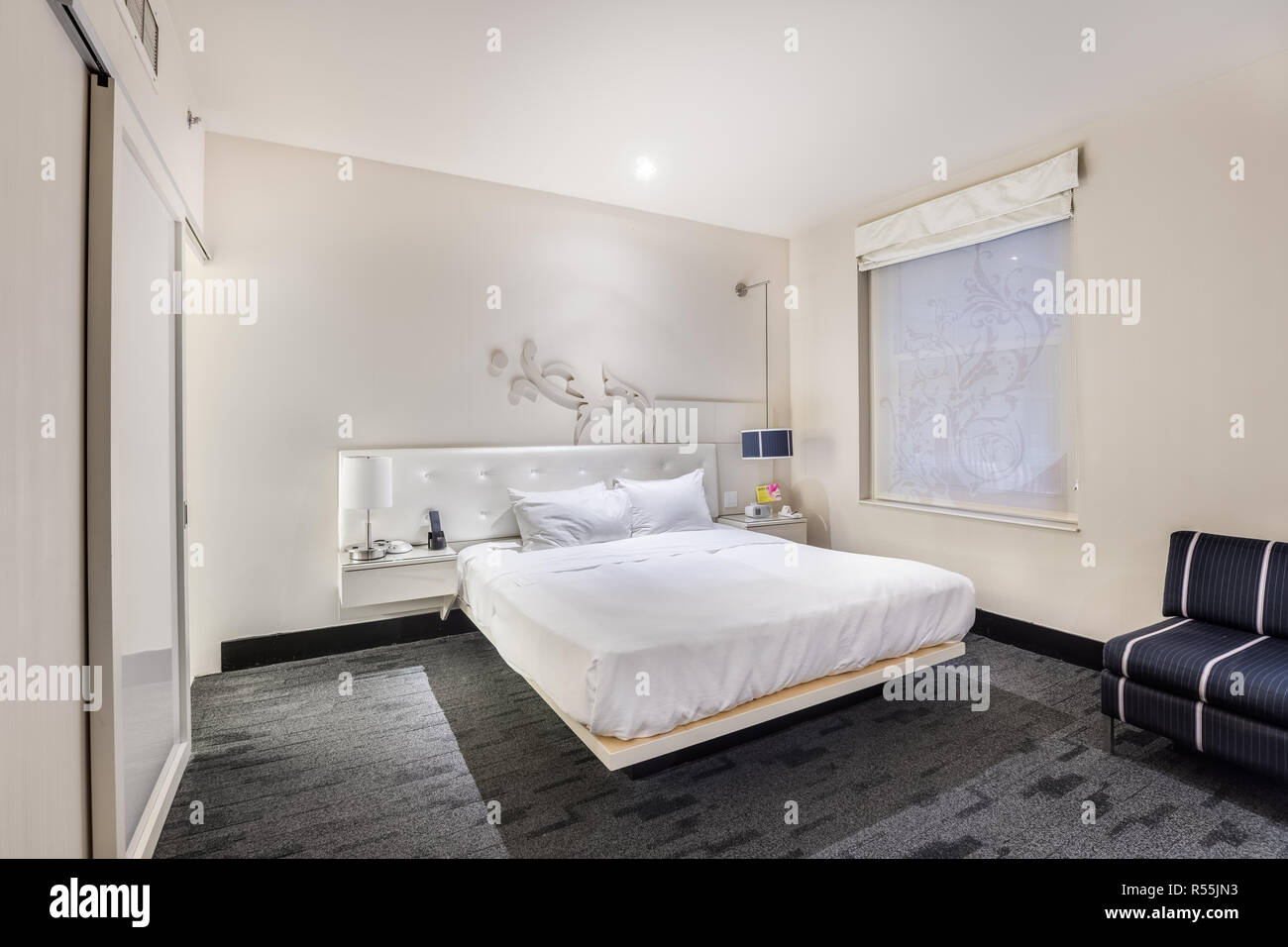 An elegant bedroom in the W Chicago - City Center hotel featuring a white bed with an overhead light shining down and artwork on the wall. Stock Photo