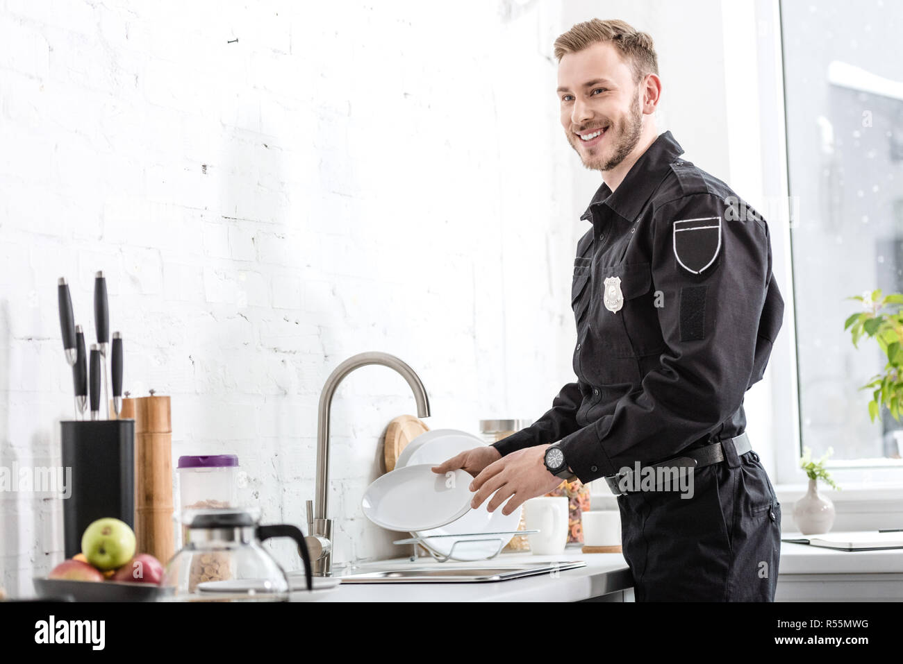 Handsome police officer smiling and washing plate at kitchen Stock Photo -  Alamy