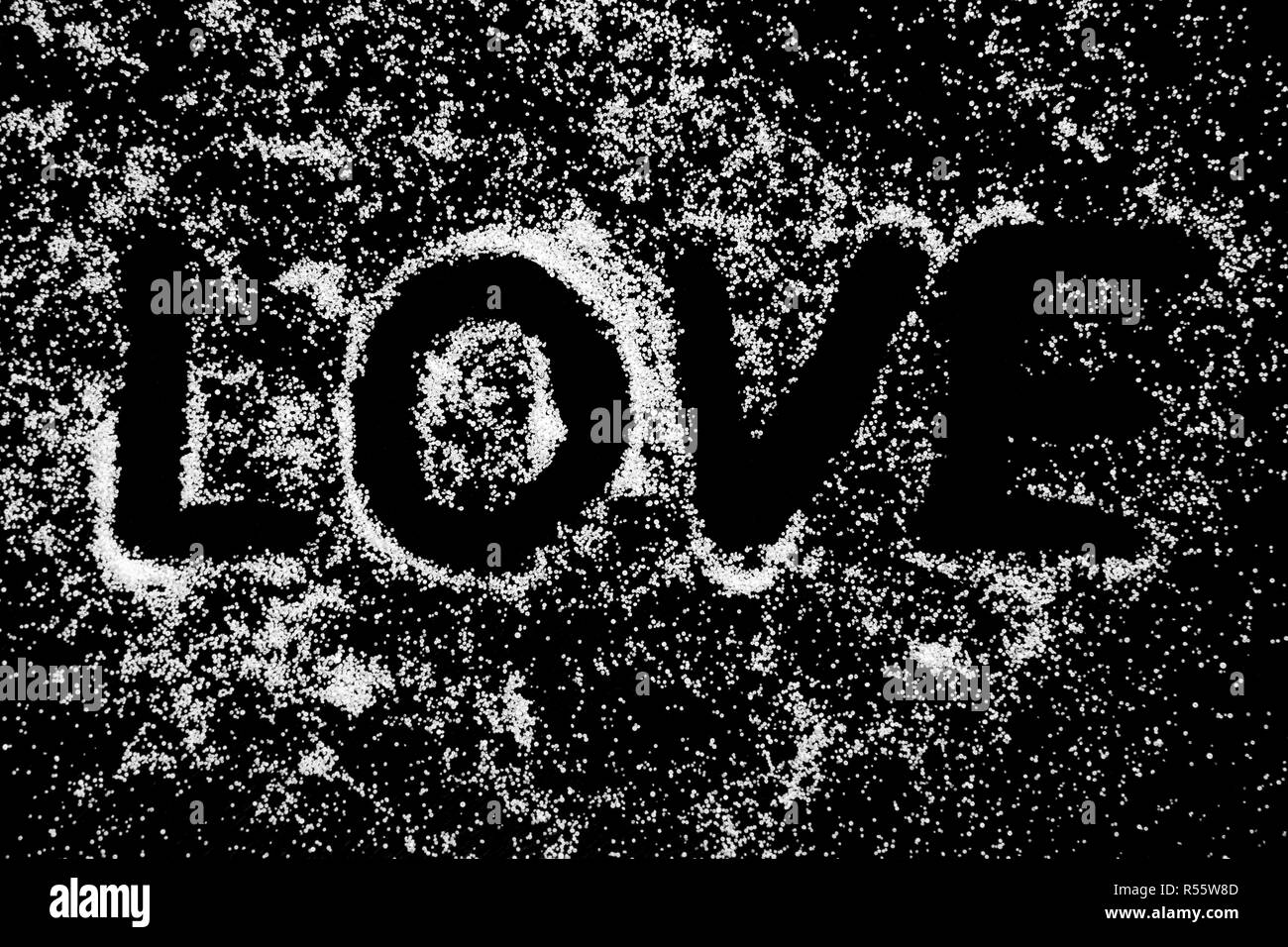 Love word symbol drawing by finger on white snow salt powder on black background. Capital letters. Romantic St. Valentines Day holidays concept with place for text. Copy space. Stock Photo
