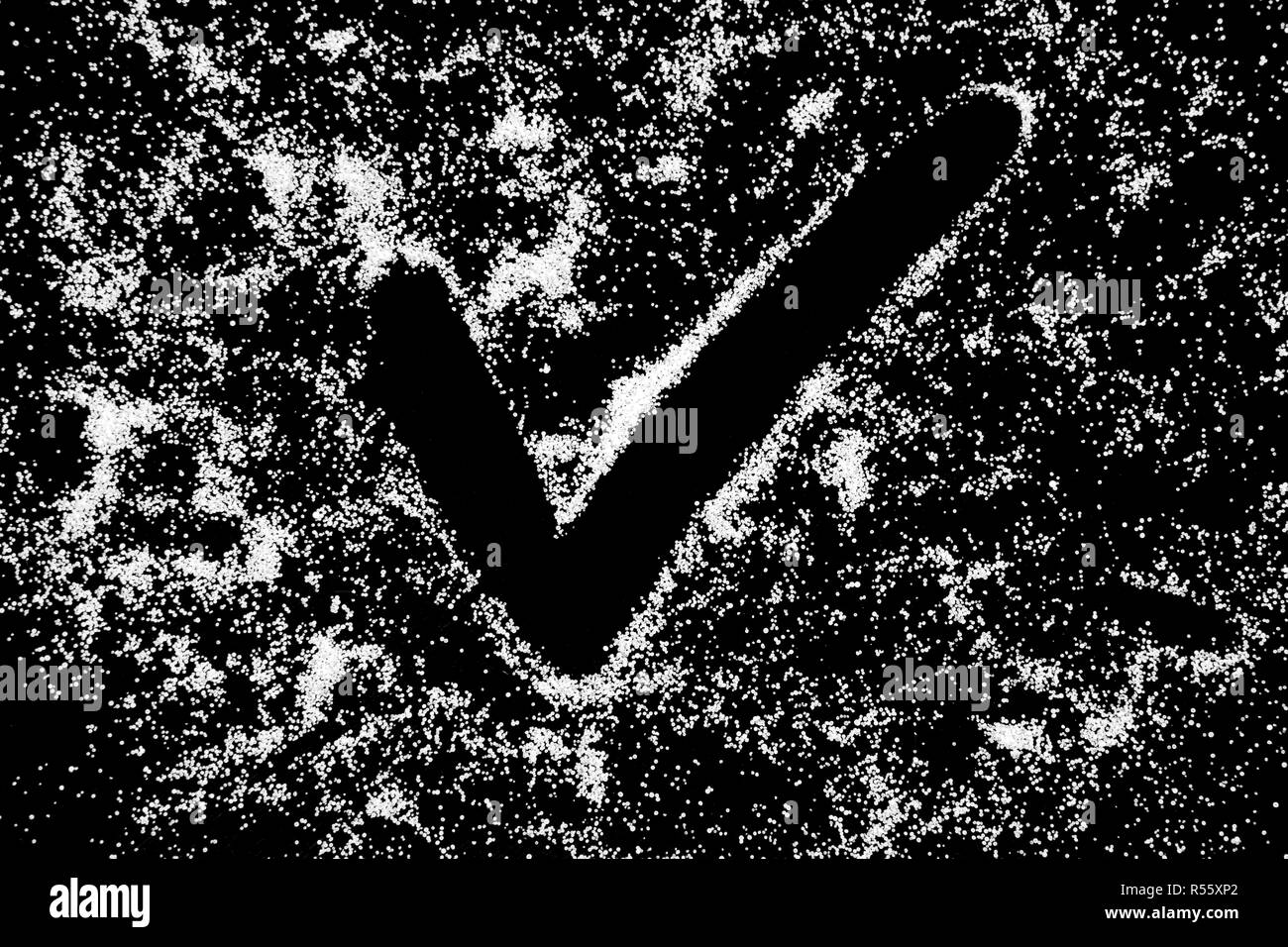 Checking mark symbol drawing by finger on white snow salt powder on black background. Tick concept with place for text. Copy space. Stock Photo