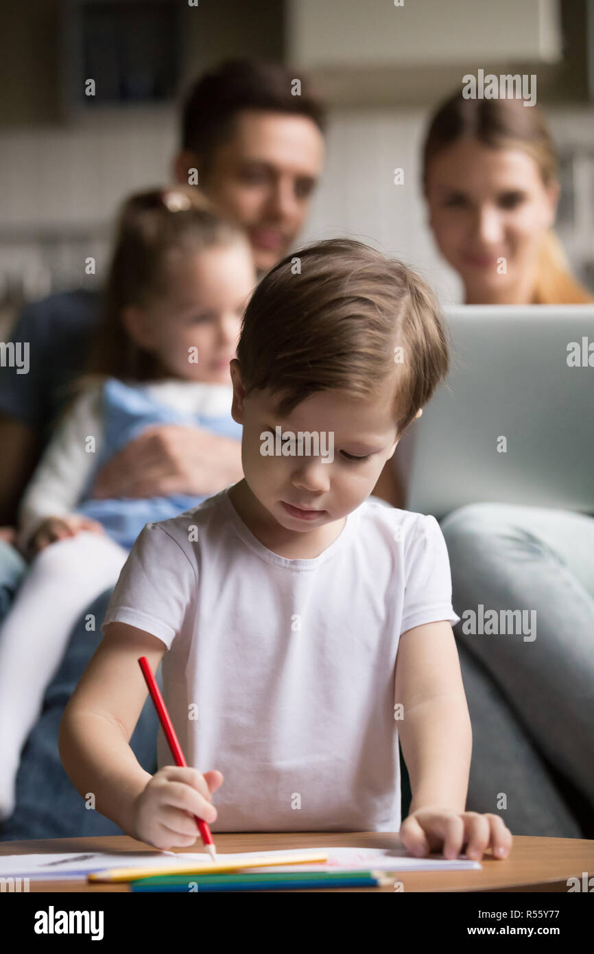 Little boy drawing while parents playing with daughter Stock Photo