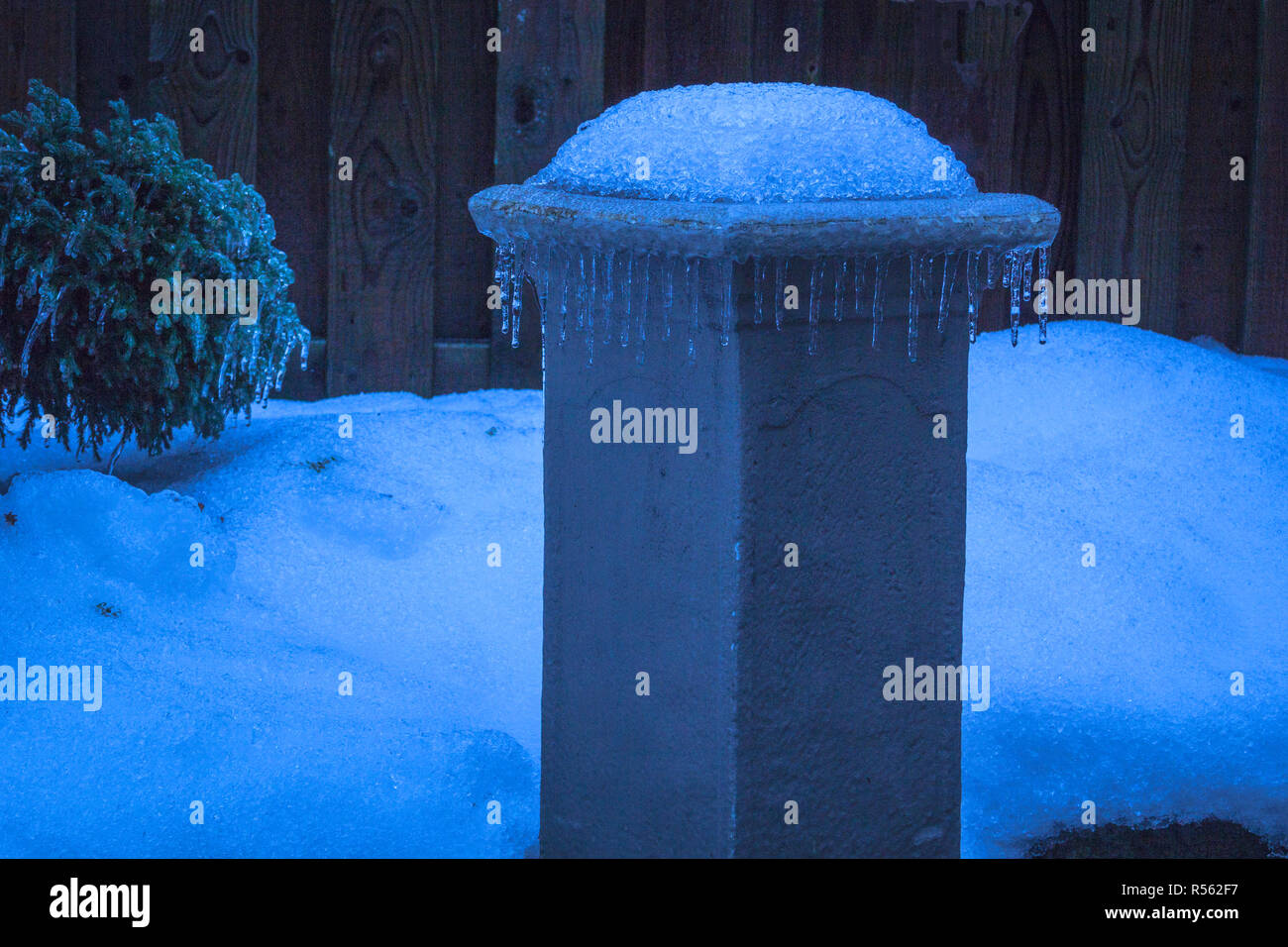 Row of icycles formed on the edge of a garden pedestal in winter. Ontario, Canada Stock Photo