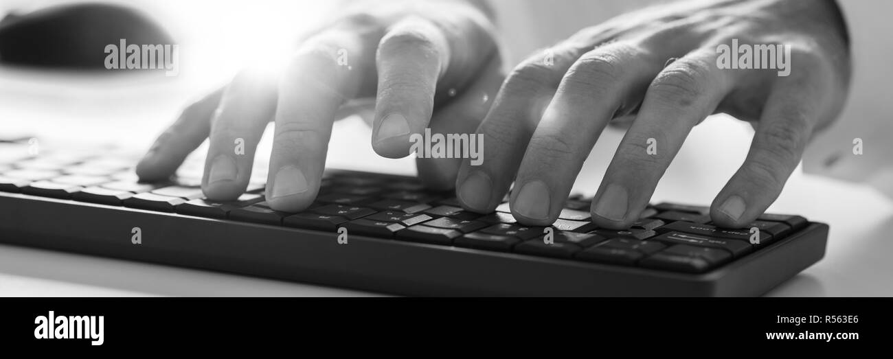 Wide view monochrome image of male hands typing on computer keyboard. With lens flare. Stock Photo