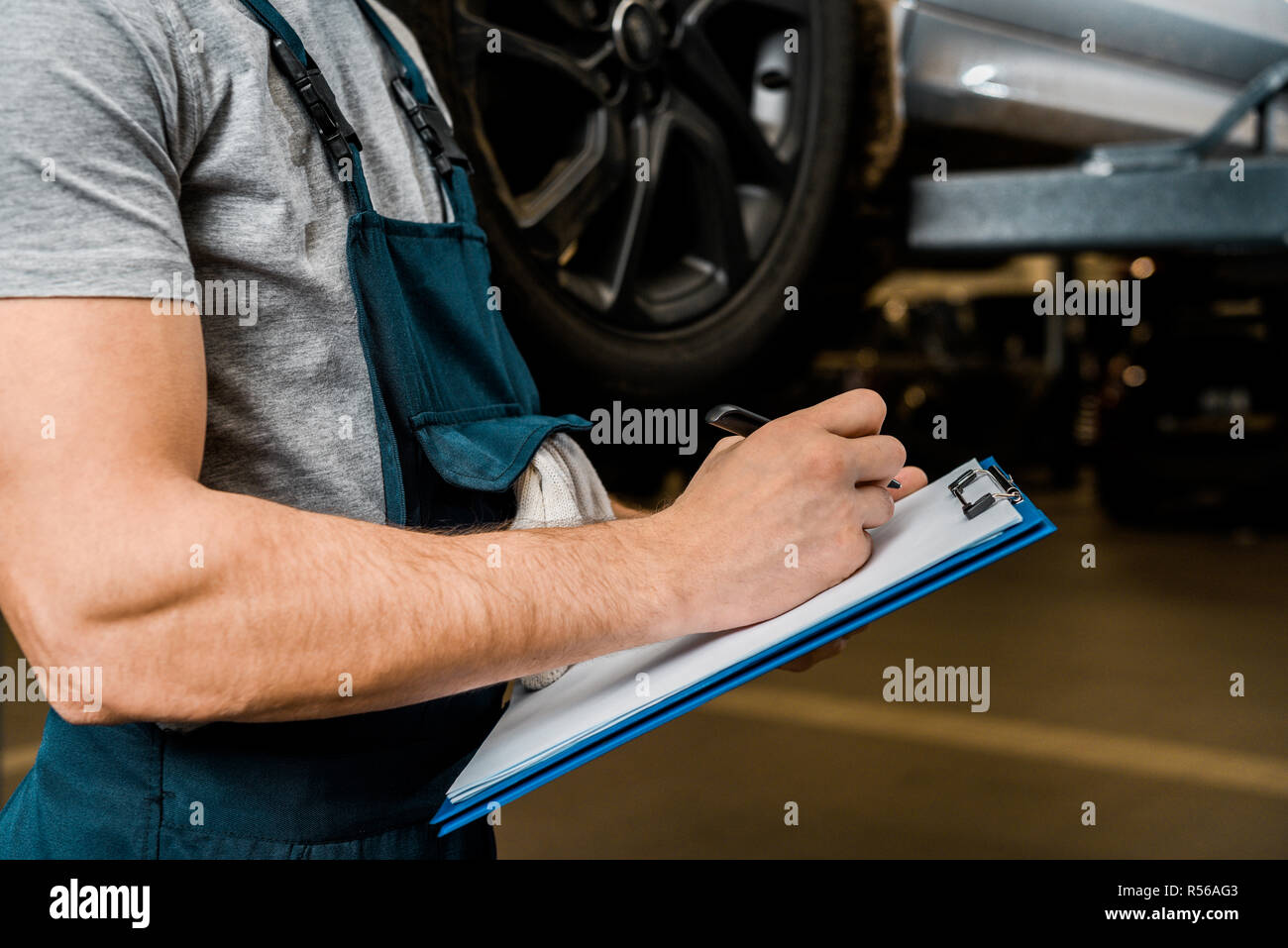 cropped shot of repairman with notepad checking car wheels at auto repair shop Stock Photo