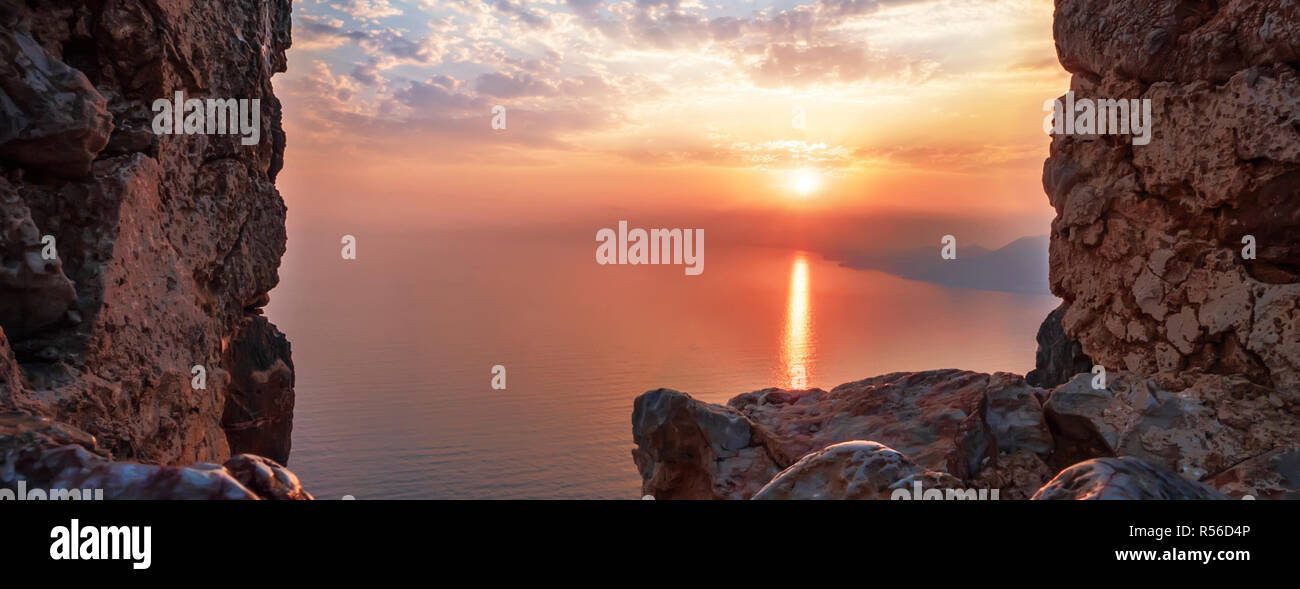 View of sunset on sea view through window in fortress with reflection on stones and shape sun rays clouds. Holiday vacation travel seascape Toned land Stock Photo