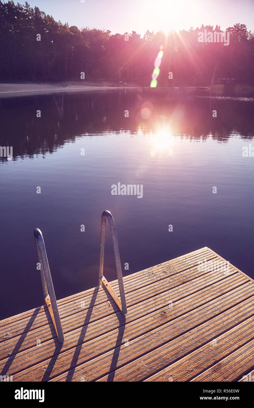 Vintage toned picture of a lake pier at sunset with lens flares. Stock Photo