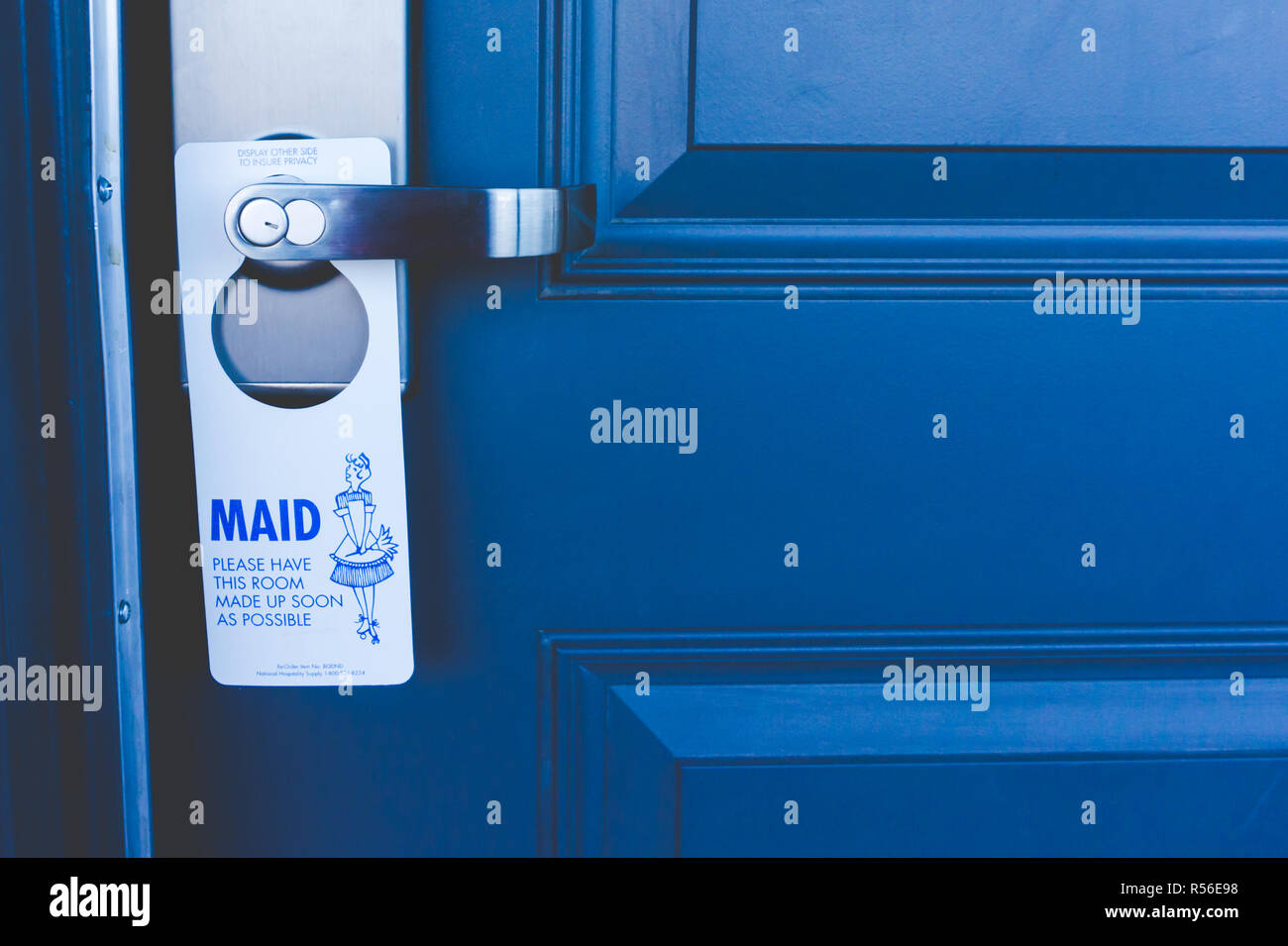 Close up of blue hotel room door with 'Maid, please' sign posted on the door handle. Stock Photo