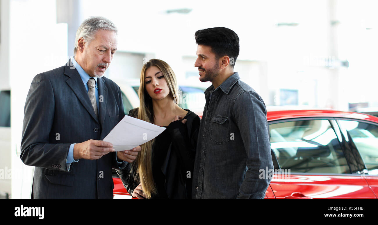 Car dealer reading a contract to a couple in an auto showroom Stock