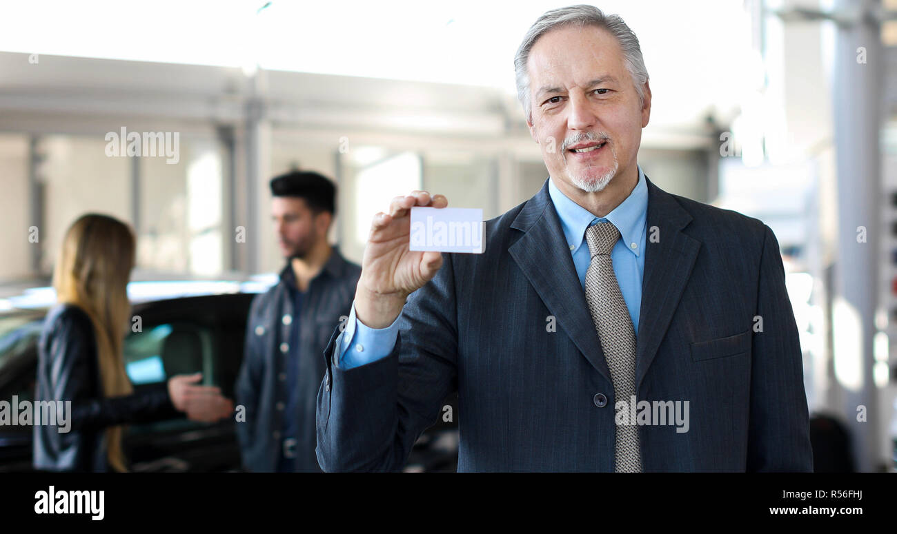 Happy male car dealer holding a business card Stock Photo - Alamy