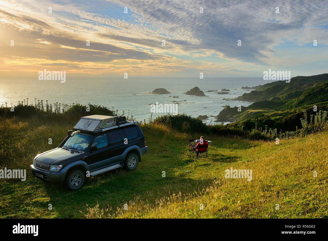 Woman sitting with off-road vehicle at the coast, Pacific, Pumillahue, Island Chiloé, Chile Stock Photo