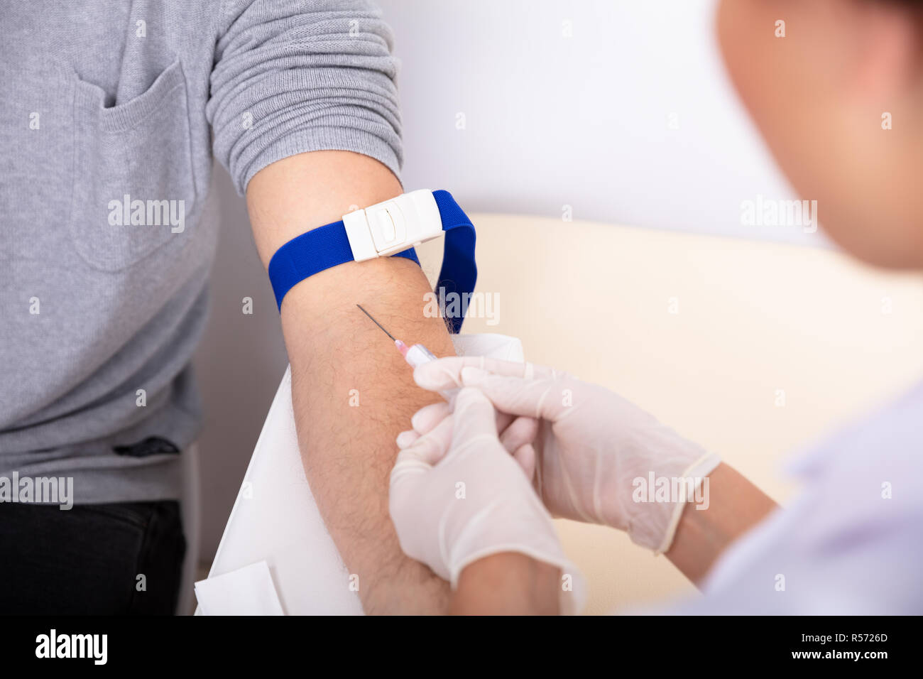 Close-up Of Doctor Injecting Syringe In Patient's Arm To Collect Blood Sample Stock Photo