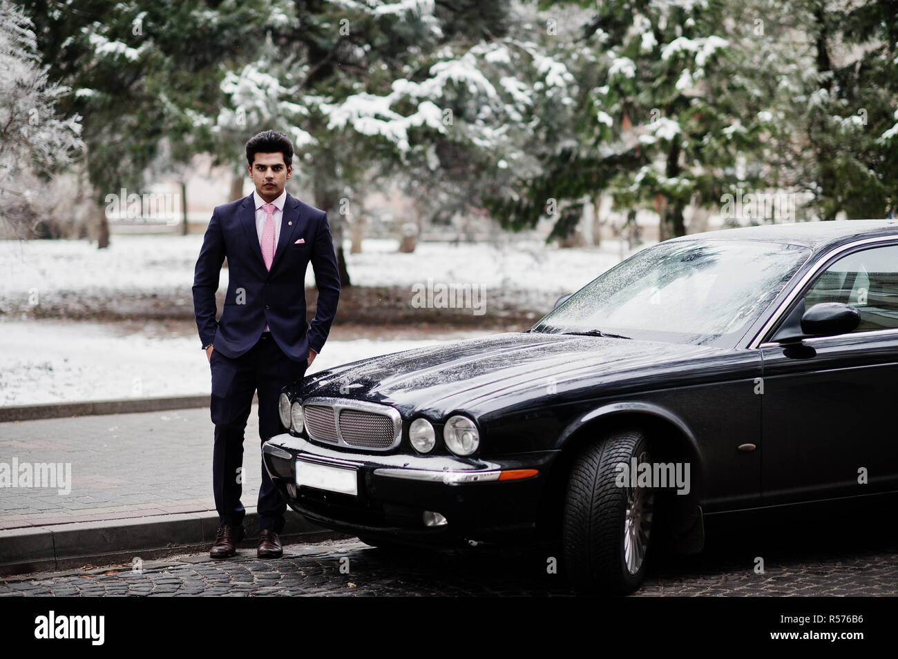 Elegant indian macho man model on suit and pink tie posed against black classic car. Stock Photo