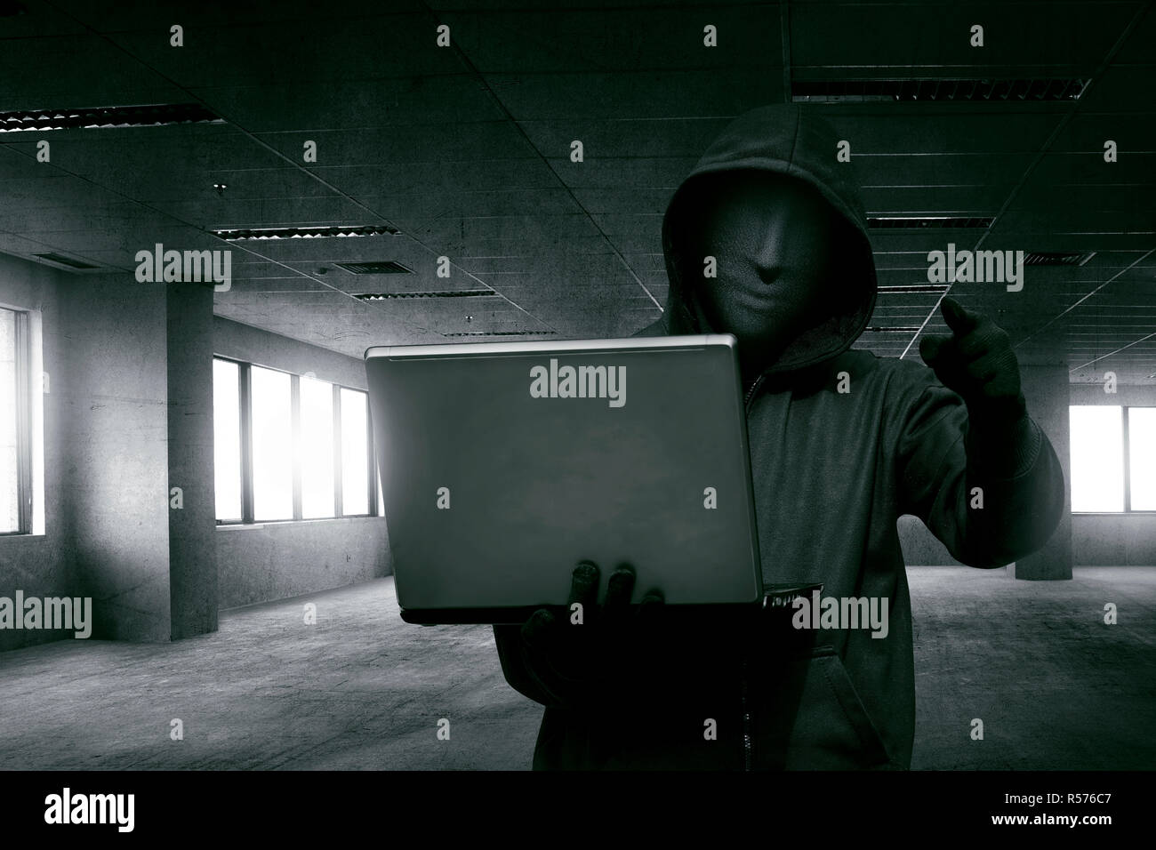 Hacker man with anonymous mask holding laptop while standing Stock Photo