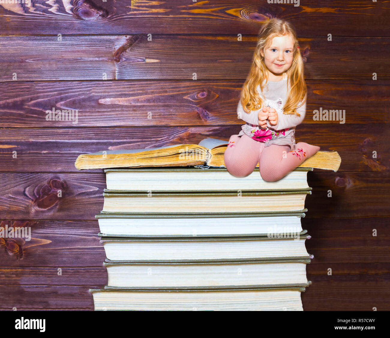 Little girl sitting on stack of books Stock Photo - Alamy